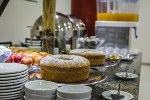 A buffet setup with a variety of food items including a large bundt cake, apples, and other dishes on trays.