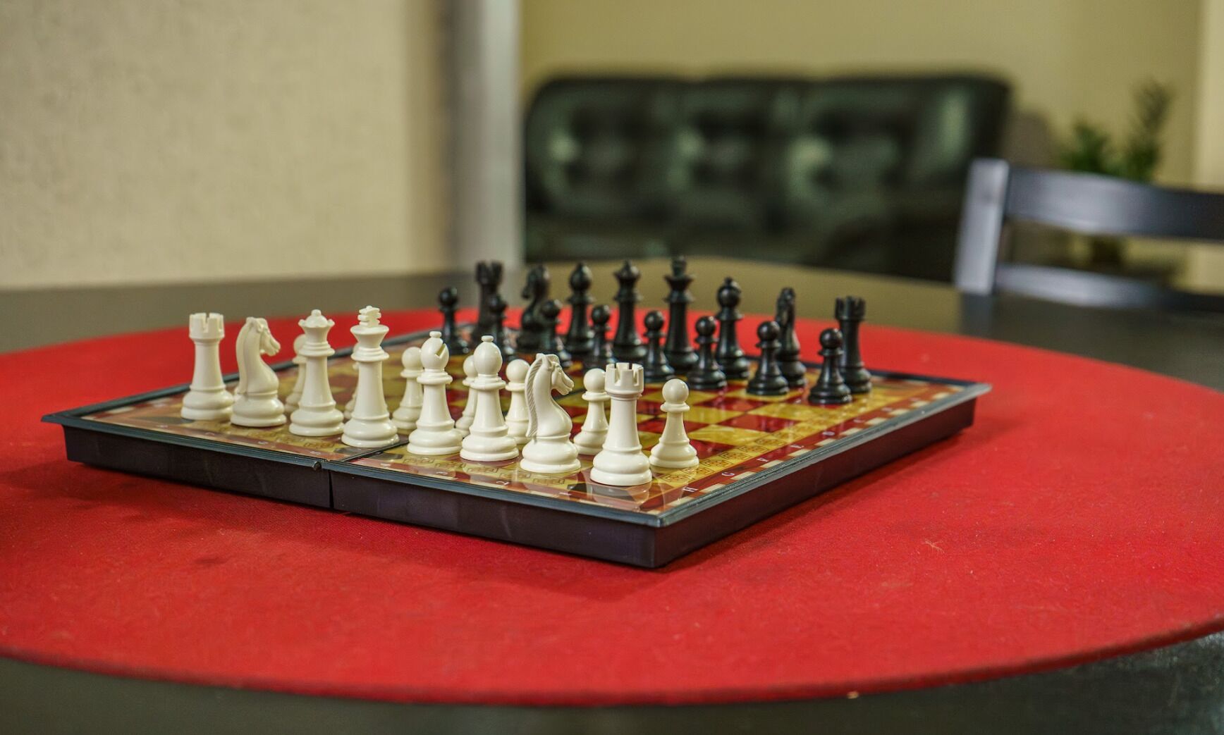 A chessboard on a red table with a couch and a chair in the background.