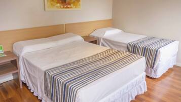 Habitación de hotel con dos camas individuales, cada una con una colcha a rayas, un cabecero de madera y una mesita de noche con lámpara.