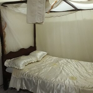 A single bed with a white bedspread and two pillows, a wooden headboard, and a canopy with a white cloth hanging from it.