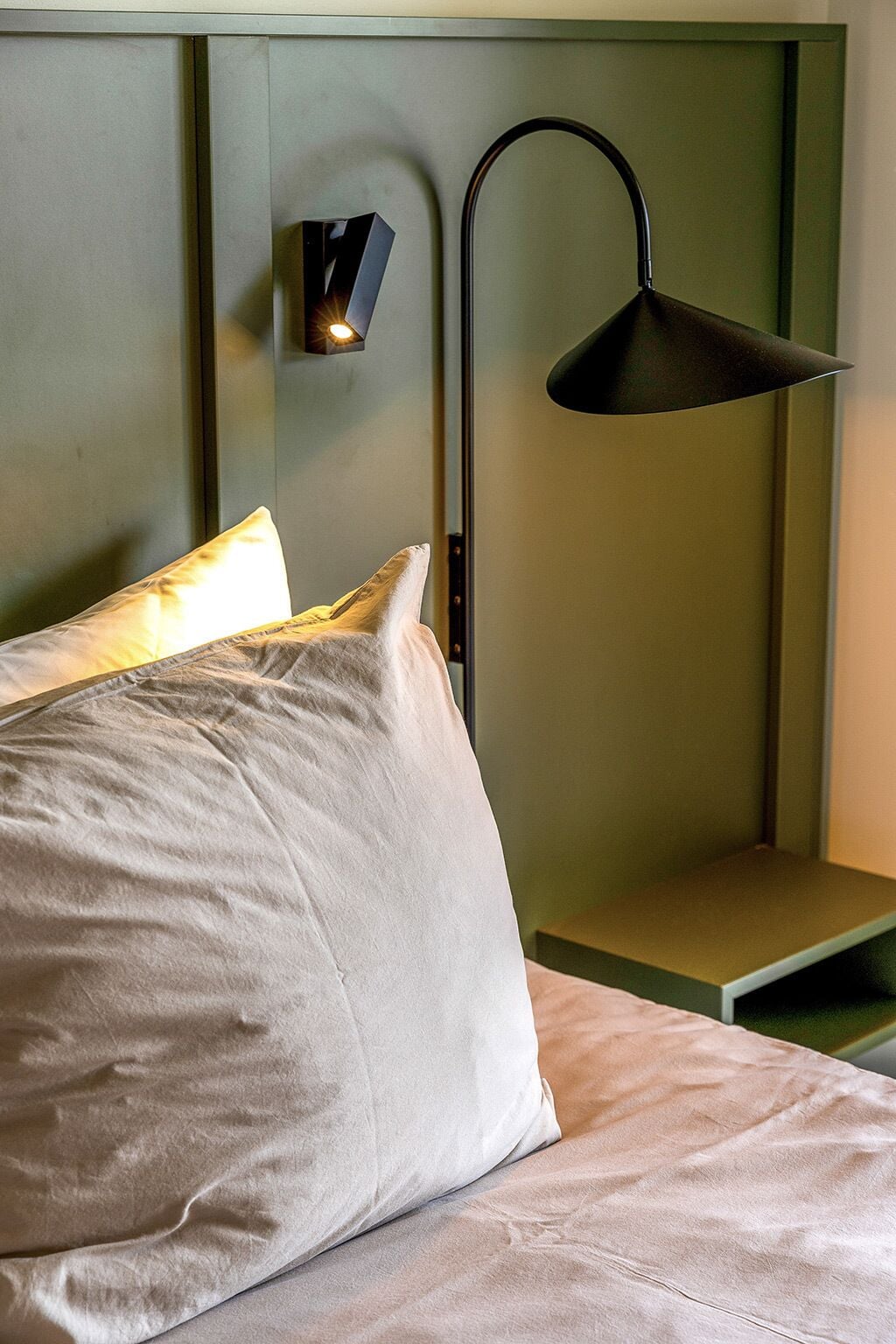 A bed with pillows and a nightstand with a lamp.