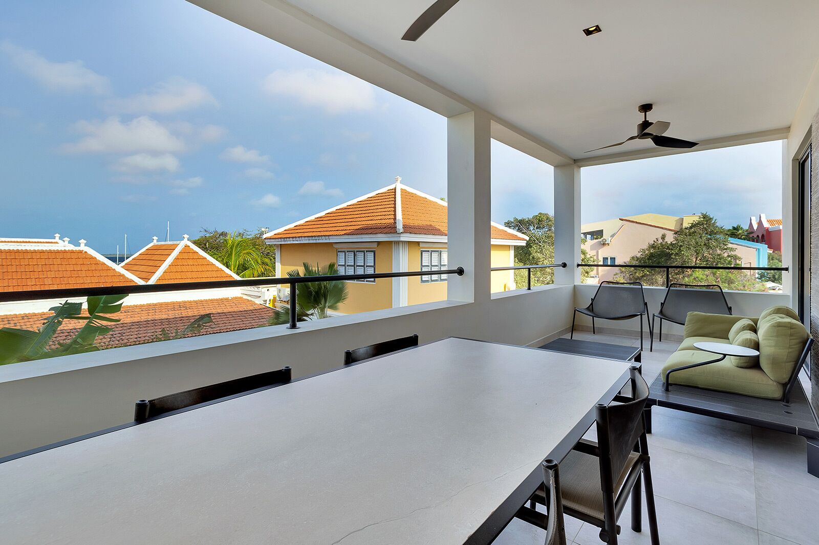 Ein Balkon mit Tisch und Stühlen, einem Deckenventilator und Blick auf angrenzende Häuser.