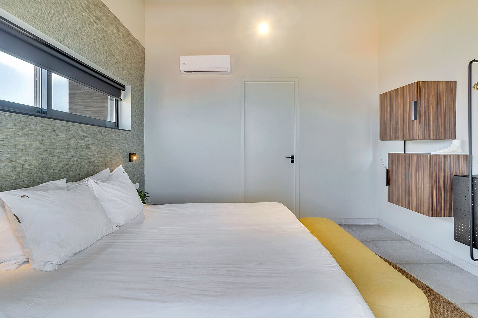 Une chambre moderne avec un grand lit, une fenêtre, un appareil de climatisation et des armoires encastrées en bois.