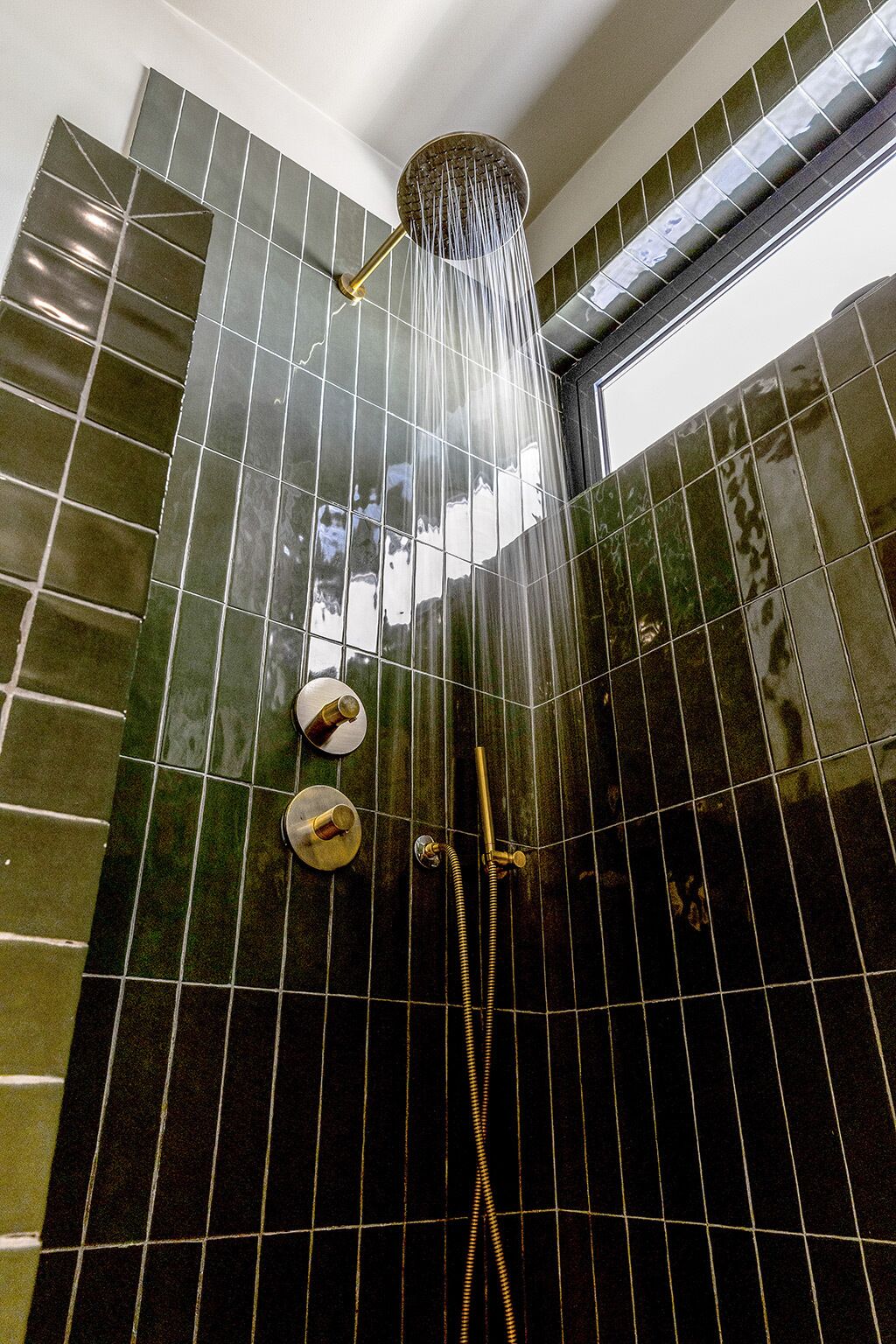 A shower with multiple nozzles and a handheld showerhead, set against a tiled wall with a grid pattern.