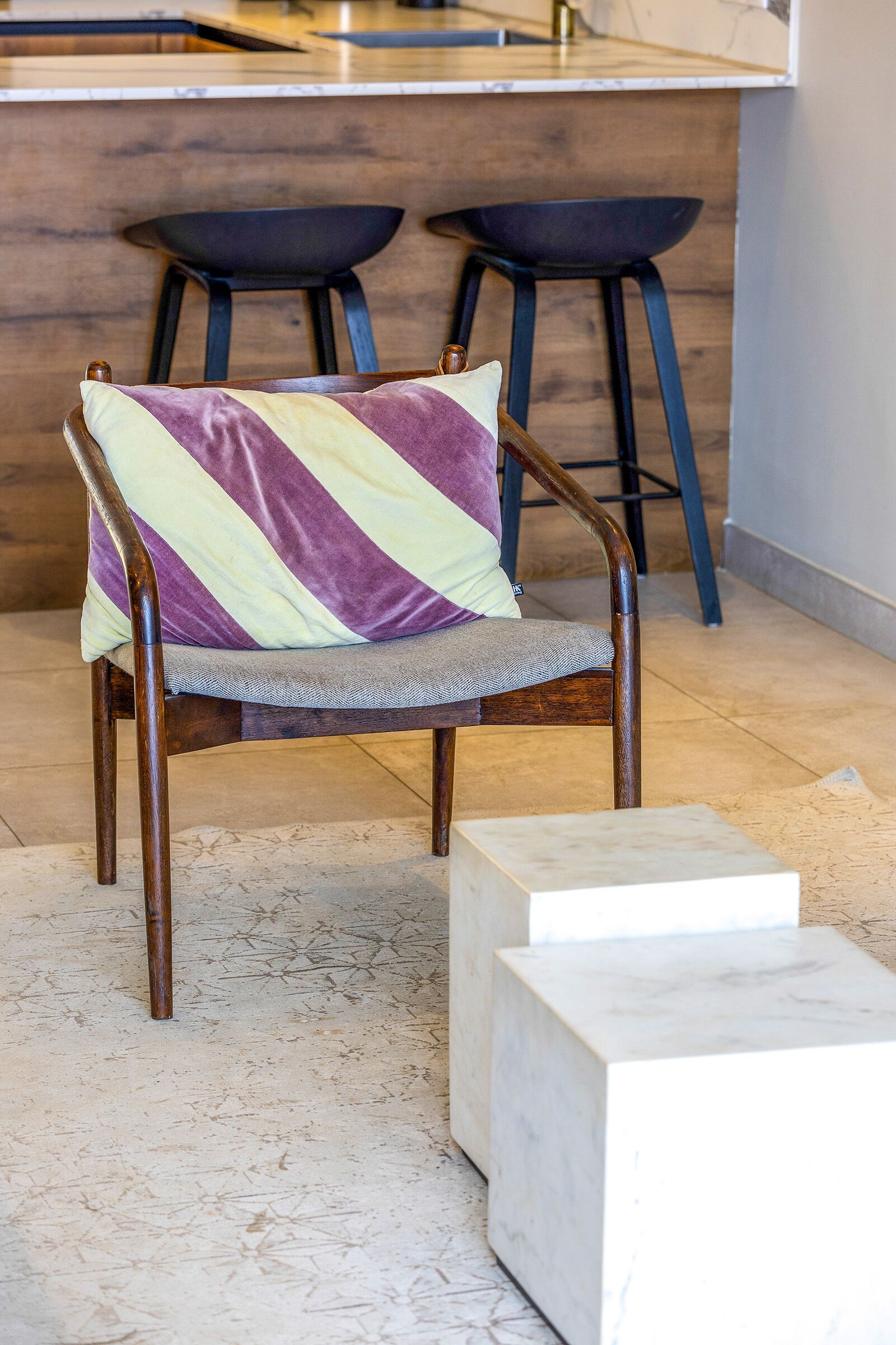 A chair with a striped cushion, a marble block, and two stools in a kitchen area.