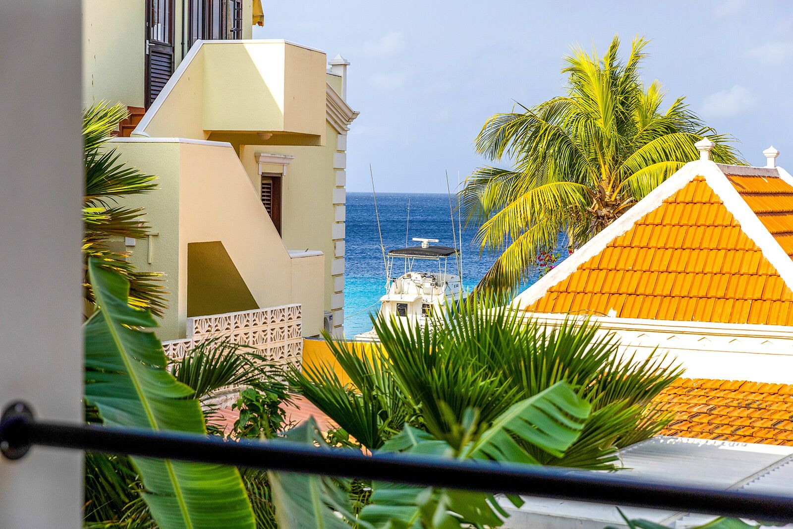 A coastal view with a boat docked near a building with a yellow roof and a balcony overlooking the sea.
