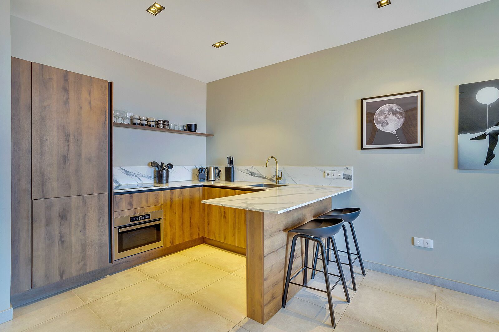 A modern kitchen with a wooden island, bar stools, and a marble countertop.