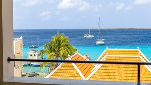 Un balcón con vista al mar, un velero y una palmera.
