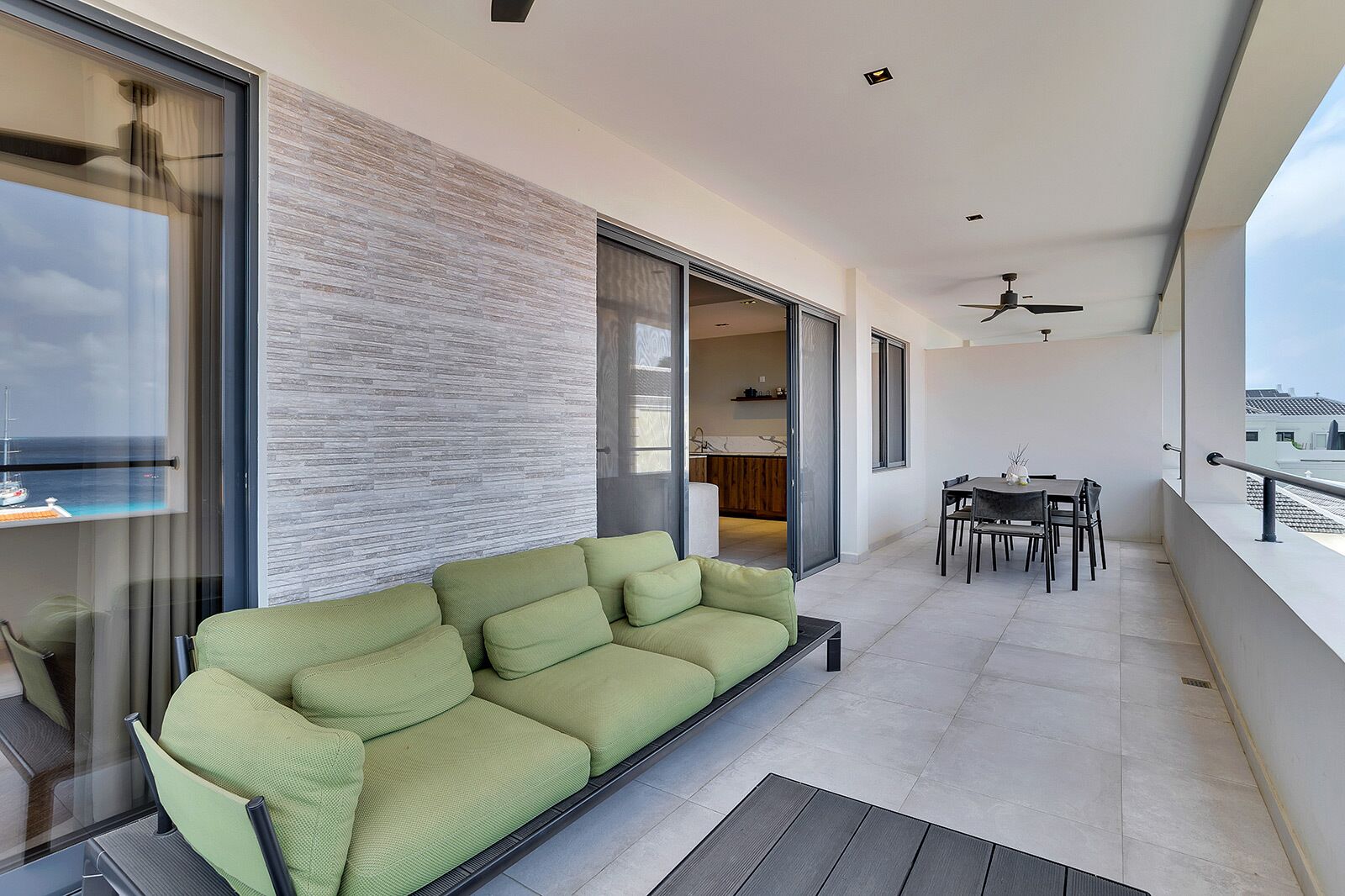 A modern living area with a green sofa, a dining table with chairs, and a view of the sea through large windows.
