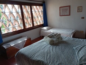 Une chambre avec deux lits, une commode en bois et une fenêtre ornée d’un treillis en bois.