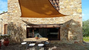 Un bâtiment en pierre surmonté d’une grande voile d’ombrage en bois qui recouvre une terrasse.