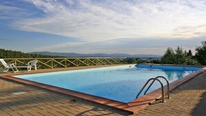 Une piscine rectangulaire dotée d’une terrasse en bois et de rampes en métal, entourée d’arbres et bordée par un paysage montagneux.