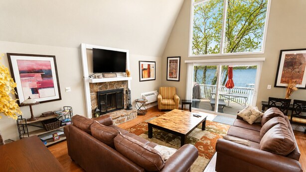 A living room with a fireplace, leather sofas, a coffee table, and a large window overlooking a deck.