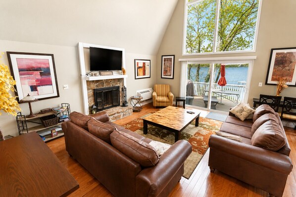 A living room with a fireplace, leather sofas, a coffee table, and a large window overlooking a deck.