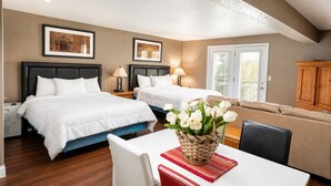 A hotel room with two beds, a dining table, a sofa, and a basket of flowers.