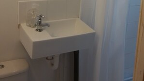 A bathroom with a white sink, a mirror above it, and a shower curtain. - SMALL STUDIO TO RENT (tottenham)