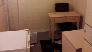 A small, compact room with a white refrigerator, a wooden table, and a chair. - SMALL STUDIO TO RENT (tottenham)