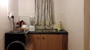 A compact kitchen with a sink, a microwave, and a small countertop. There is a window with a curtain, and a basket with items on the counter. - SMALL STUDIO TO RENT (tottenham)
