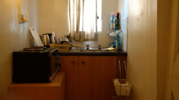 A compact kitchen with a sink, a small refrigerator, and a window with curtains. - SMALL STUDIO TO RENT (tottenham)