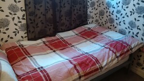 A bed with a plaid blanket, floral wallpaper, and a dark curtain. - SMALL STUDIO TO RENT (tottenham)