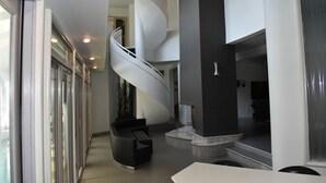 Un interno moderno con una scala a chiocciola, una zona salotto e vista sull'esterno.