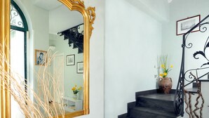 Un escalier au plancher sombre, un grand miroir décoratif et un vase contenant des plantes séchées.