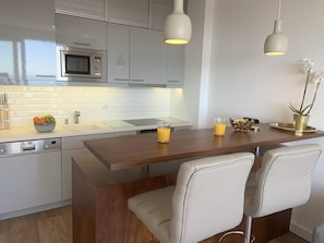 A modern kitchen with a wooden island, white chairs, and a dining area. - Panoramic Ocean and Cascais View Apartment with Balcony (Cascais)