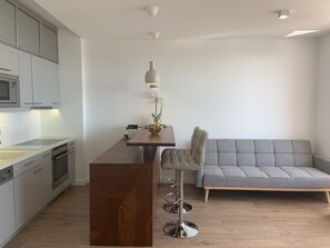 Et moderne køkken med en træø, barstole, en grå sofa og en hængende lampe.