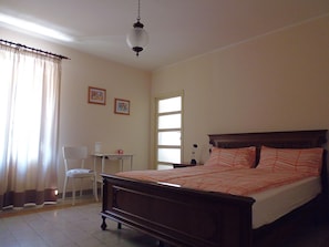 Une chambre avec un lit en bois, un bureau et une chaise. Deux tableaux encadrés sont accrochés au mur.