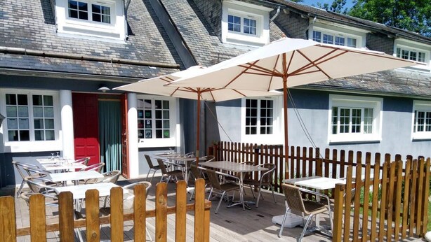 En udendørs patio med træborde og stole, et træhegn og en stor parasol.