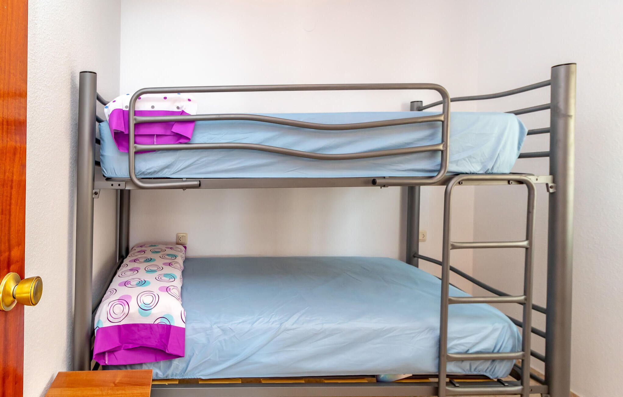 Ein Etagenbett mit einem unteren und einem oberen Bett, jeweils mit blauer Bettwäsche.