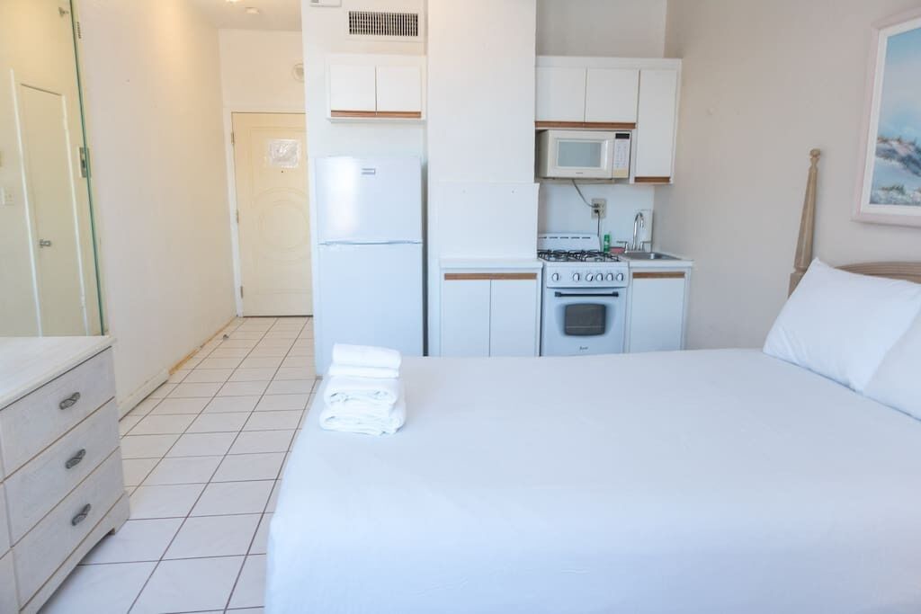 Quarto de hotel com cama, pequeno espaço de cozinha, micro-ondas, frigorífico e armário de madeira.