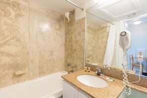 A bathroom with a granite countertop sink, a mirror, a handheld hair dryer, and a shower with beige tiles. - 651 Studio Apartment Hollywood Beach (Hollywood)