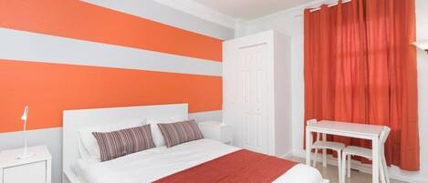 A bedroom with a bed, bedside table, and a desk with chairs.