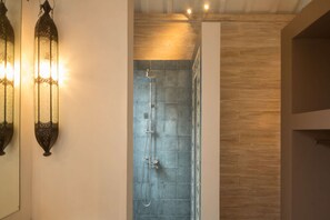 Una ducha con pared de azulejos, suelo de madera y luces fijadas a la pared.