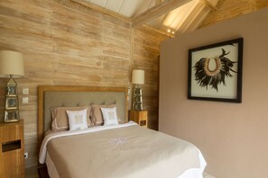 Un dormitorio con techo de madera, una cama grande con edredón color beige, dos lámparas de noche y una obra enmarcada en la pared.