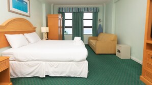 Hotellihuone, jossa on suuri sänky, tuoli, vaatekaappi ja näkymä merelle.