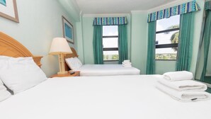A hotel room with two beds, a nightstand with a lamp, and a view of palm trees through the windows. - 657 Apartment Hollywood Beach (Hollywood)