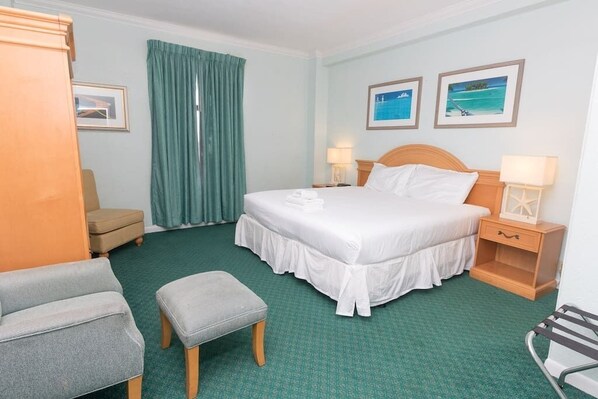 A hotel room with a large bed, a chair, an ottoman, a nightstand, and a window with curtains.
