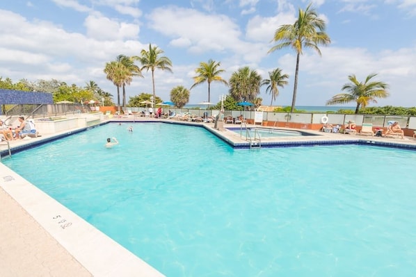 A rectangular swimming pool with clear blue water, surrounded by lounge chairs and palm trees, with a view of the ocean in the background. - 770 Ocean View Hollywood (Hollywood)