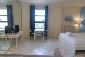 A hotel room with a bed, a desk with a TV, a chair, a table, and a window with curtains. - 778 Studio Apartment Hollywood (Hollywood)