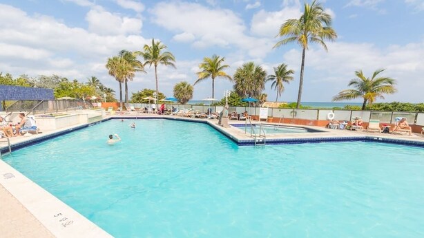 Une piscine rectangulaire à l’eau d’un bleu cristallin, entourée de chaises longues et de palmiers.