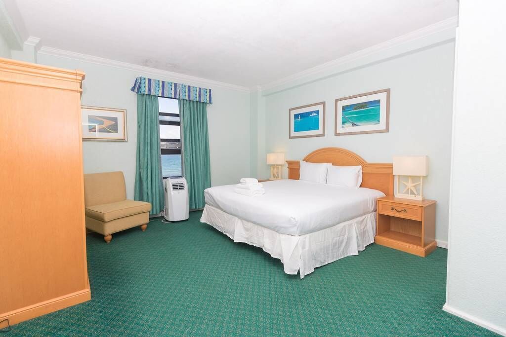 A hotel room with a large bed, a sofa, a desk, and a window with curtains.
