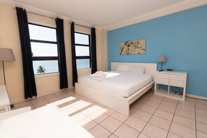 A hotel room with a bed, a nightstand, a lamp, and a view of the ocean through large windows. - 764 Ocean View Hollywood Beach (Hollywood)