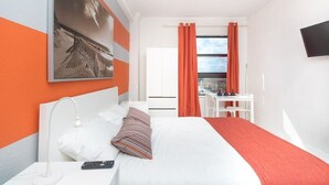 A hotel room with a bed, a desk, and a chair. There is a window with curtains, a flat-screen TV mounted on the wall, and a painting on the wall. - 737 City View Studio on the Hollywood Beach Boardwalk (Hollywood)