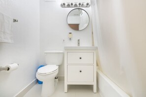 Une petite salle de bain blanche, avec des toilettes, un lavabo et un miroir.