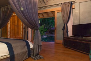 A bedroom with a bed, curtains, a television, and a view of an outdoor pool area.