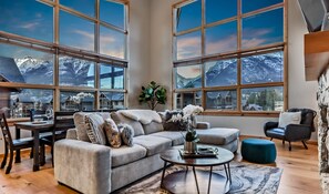 A spacious living room with large windows offering mountain views, a cozy sofa, a coffee table, and a stone accent wall.