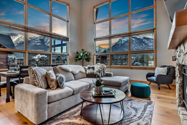 A spacious living room with a large window offering a mountain view, a cozy sofa, a coffee table, and a stone fireplace.
