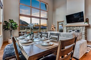 A dining area with a large window, a stone fireplace, and a flat-screen TV.